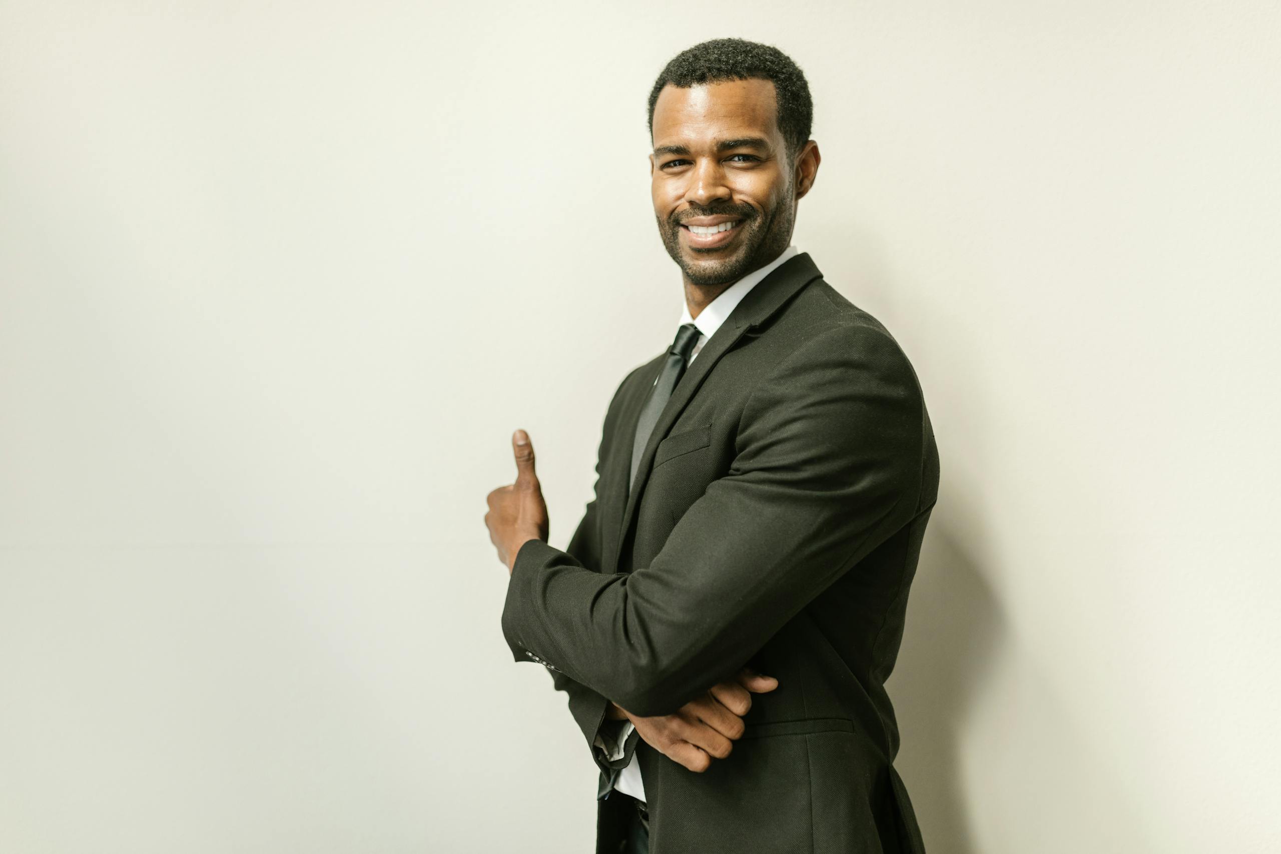 A confident African American man in a black suit, smiling against a white wall.